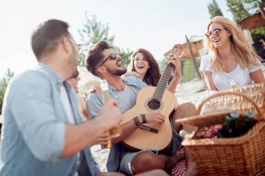 Genç çekici gitar çalmak için arkadaş sahilde otururken adam.