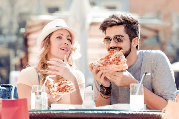 Alegre pareja joven sentada en un restaurante, comiendo pizza . — Foto de Stock