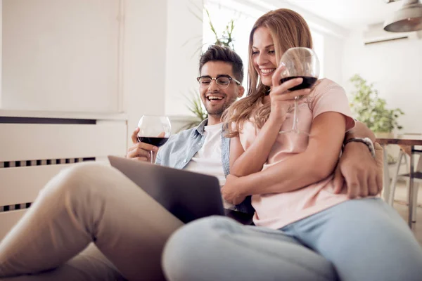 Pareja joven degustando vino y trabajando en un portátil . — Foto de Stock