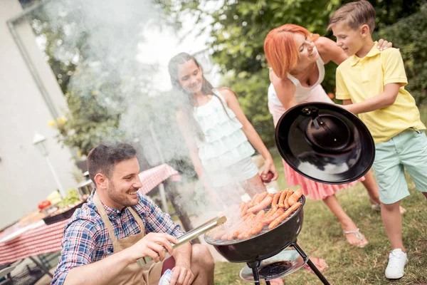 Smiling man cooking food on barbecue with family enjoying weekend in the backyard.