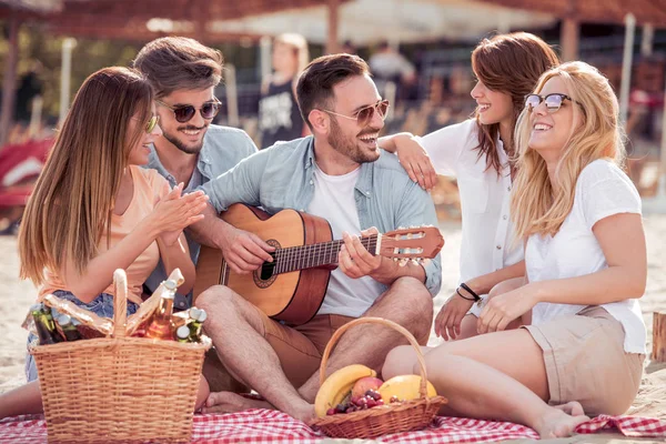 Young friends enjoying a beach party with music and drinks.Young man playing guitar with his friends.