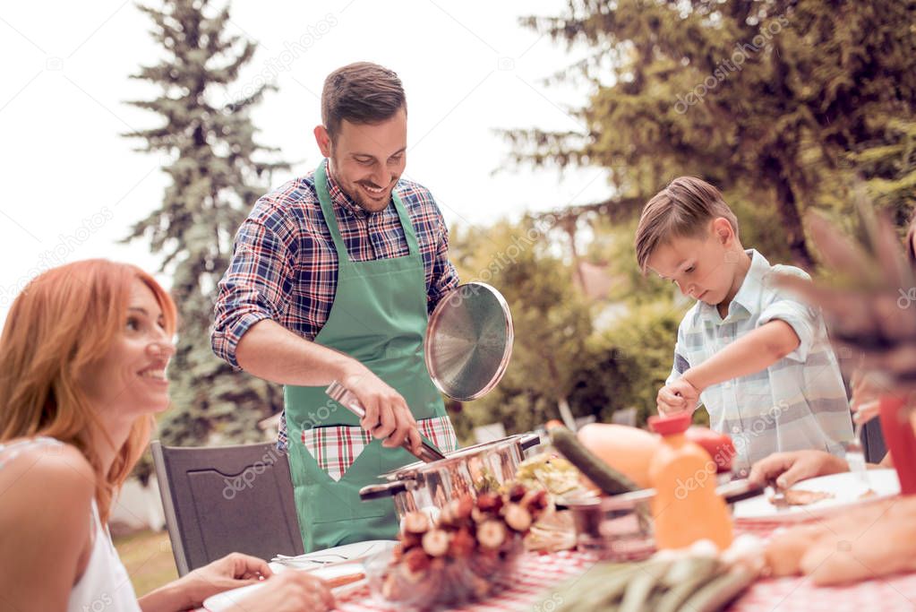 Happy young family having lunch barbecue in the garden on a sunny day.