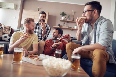 Pizza yeme ve soğuk bira içme sırasında evde TV izlerken arkadaşlar.