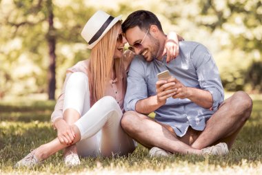 Genç çift açık bir parkta otururken akıllı telefon kullanarak. Telefon sahip yakışıklı bir adam. İnsan ve teknoloji kavramı