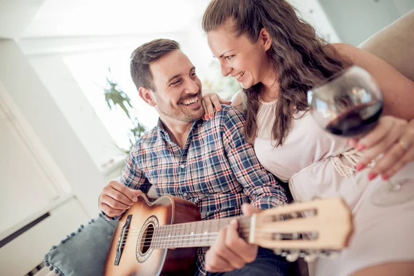 Man playing guitar in living room and woman listening, romantic moments.