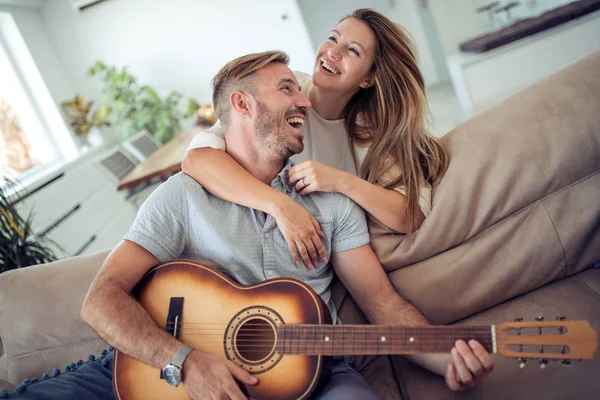 Lovers in a living room.Young couple in love sitting on the sofa while young man playing guitar in living room.