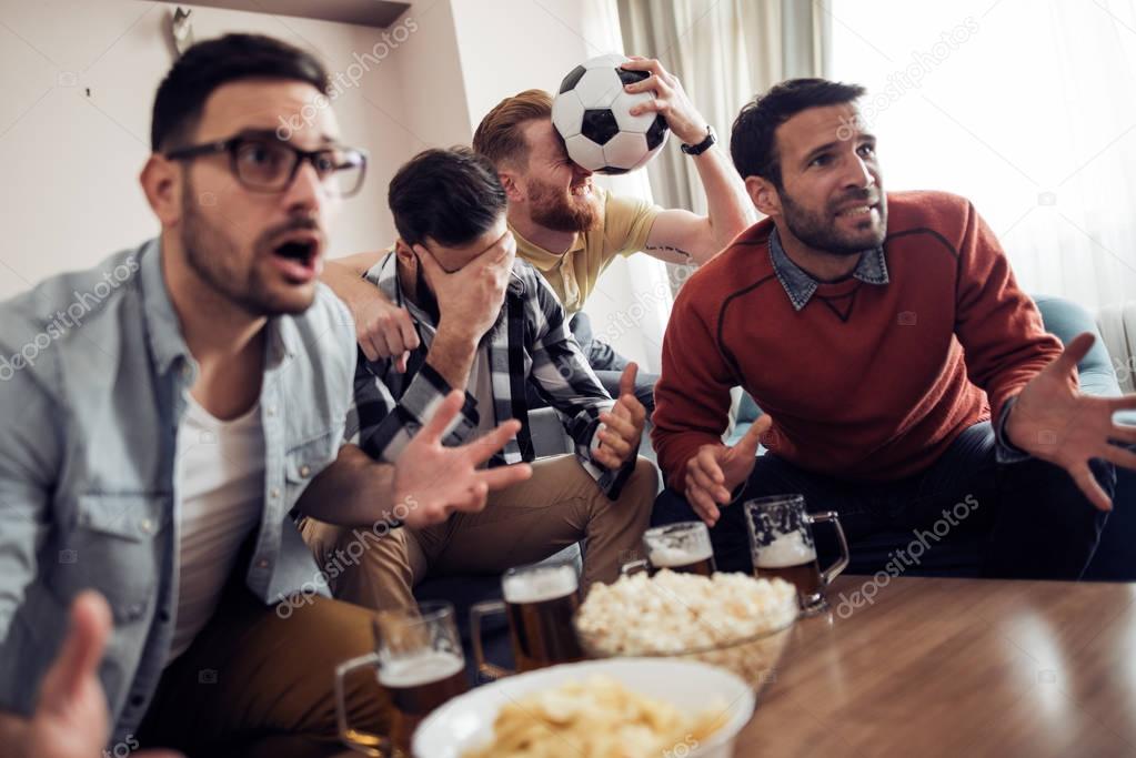 Friends watching TV at home while eating pizza and drinking some cold beer.