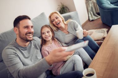 Birlikte televizyon seyreden gülümseyen genç bir aile. Evde boş zaman geçiriyorlar..