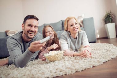 Birlikte televizyon seyreden gülümseyen genç bir aile. Evde boş zaman geçiriyorlar..