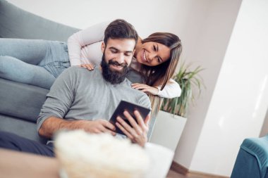 Çift satır içerik evde kanepede oturan bir Tablet üzerinde izlerken.