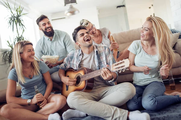 Grup arkadaşıyla birlikte evlerinde oturma odasında eğleniyor. Şarkı gülen ve birlikte müzik gitar ile mutlu gençler .