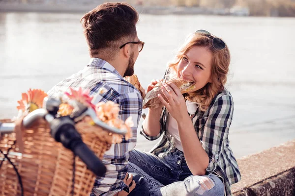 Romantic couple eating a sandwiches,rests after riding a bicycle in the background is a river.