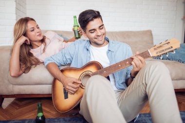 Yakışıklı adam şarkı söyleyen kız arkadaşıyla gitar evde oturma odasında