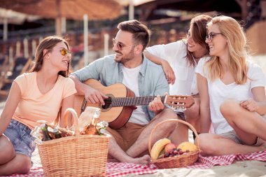 Dört arkadaş müzik ve içecekler ile sahilde piknik keyfi
