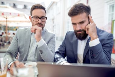 Kentsel kafede masada oturan ve dizüstü bilgisayar kullanarak iki iş adamları