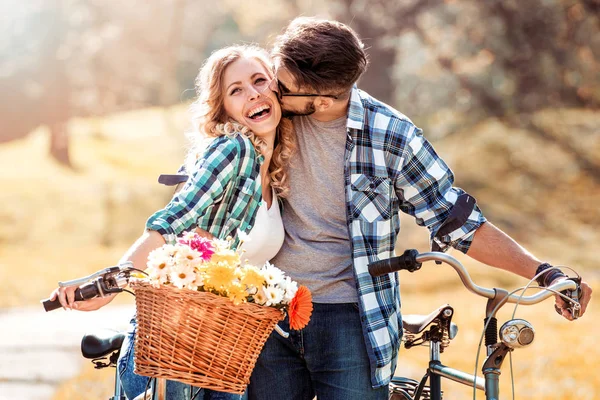 Trendy young couple riding on bikes with basket of flowers