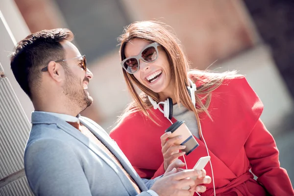Happy couple with headphones sharing music from smartphone on street
