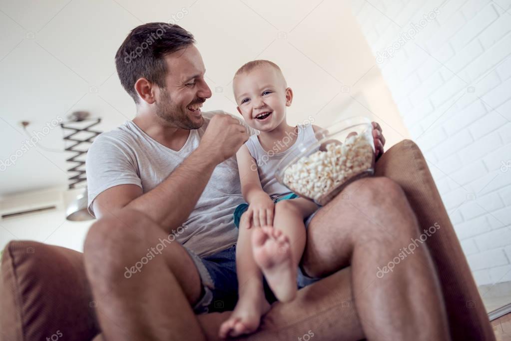 father and little son eating popcorn at home