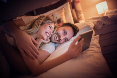 Yatak odasında tablet kullanarak çekici genç bir çift. İnsanlar, sevgi, mutluluk ve eğlence kavramı.