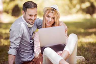 Birlikte yaz günü parkta oturan, dizüstü bilgisayar kullanarak, gülüyor, eğleniyor genç güzel mutlu gülümseyen Çift.