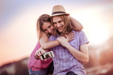 Gün batımında akıllı telefon ile mutlu Romantik Çift alarak fotoğraf kendilerini. Erkek ve kadın aşık.