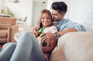 Oturma odasında kanepede oturup, bira holding ve gülümseyen genç Çift.