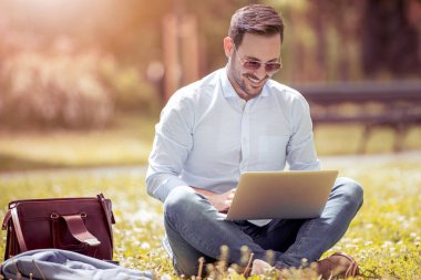 Dizüstü enjoing parkta çalışma ile genç adam.