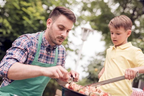 Leisure,food,people and holidays concept-man cooking meat on barbecue grill with his son,for his family at summer outdoor party