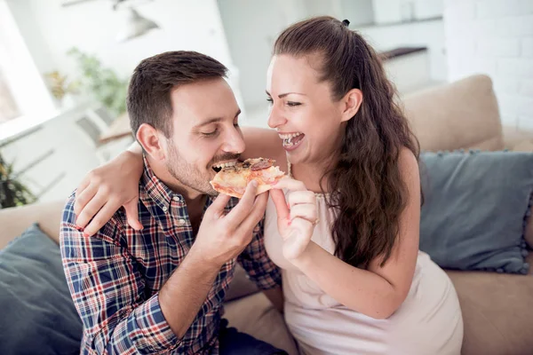 Beautiful young couple eating pizza and they are watching tv.