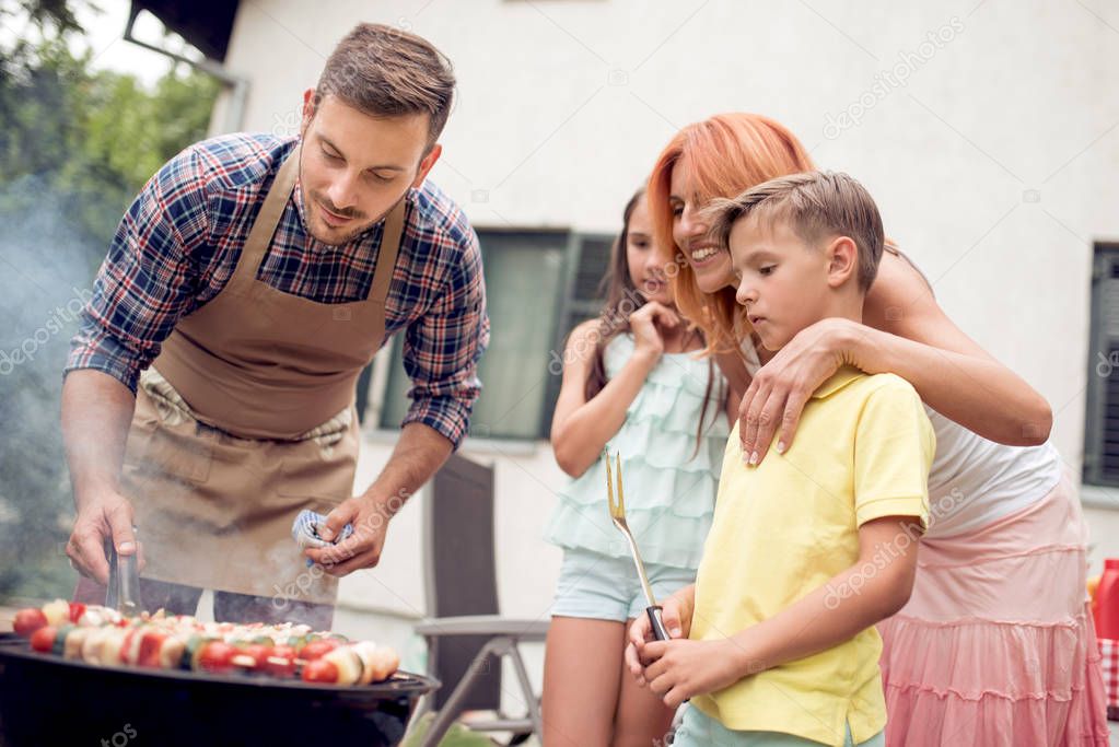 Happy father doing barbecue with her daughter,son and wife on a sunny day