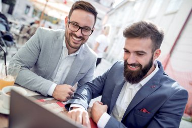 Kentsel kafede masada oturan ve dizüstü bilgisayar kullanarak iki yakışıklı iş adamları.