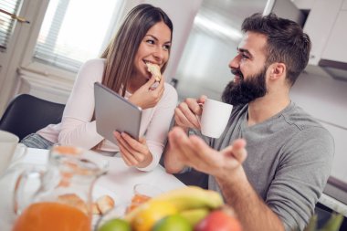 Genç mutlu çift modern dairede oturuyor ve birlikte kahvaltı yapıyorlar..