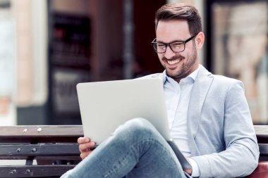 Bankta oturan ve Şehir Parkı içinde laptop izlerken işadamı gülümseyen.