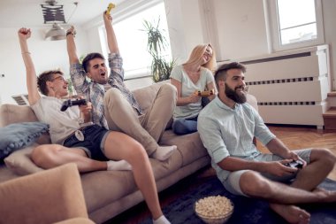 Modern apartmanda oturuyor ve video oyunları oynarken yetişkin arkadaş grubu.