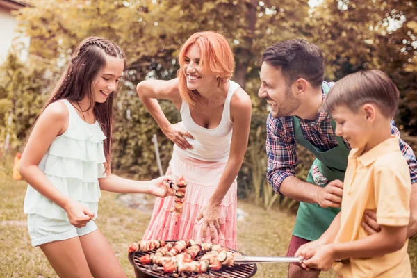Leisure,food,people and holidays concept-man cooking meat on barbecue grill for his family at summer outdoor party.