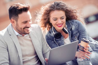 Dizüstü bilgisayar kullanarak, söz ve açık havada otururken gülümseyen güzel genç Çift.