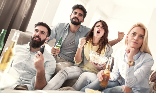 Cheerful group of friends watching football game on tv,having fun at home.