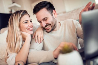 Genç çift kanepede dizüstü bilgisayarla dinleniyor. Aşk, mutluluk, insanlar ve eğlence konsepti..