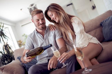 Güzel çift şarap içmek, konuşmak ve evde kanepede gülümseyen.