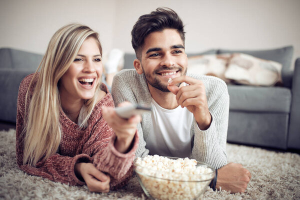 Happy young couple watching tv at home,man eating popcorn.