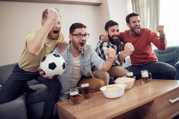 Group of friends watching soccer game on television, celebrating goal.