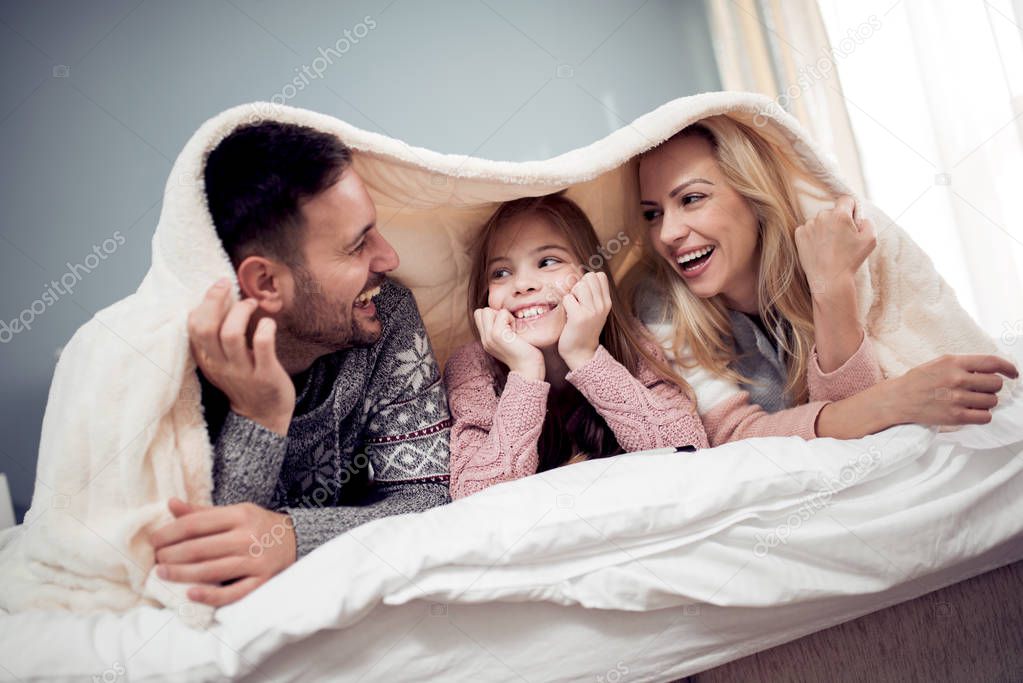 Mom, dad and daughter lying under blanket ,watching movie and having wonderful  time.