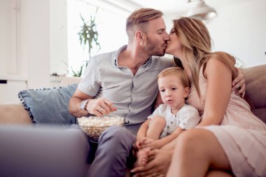 Anne ve küçük oğlu kanepede oturan ve evde patlamış mısır yemek