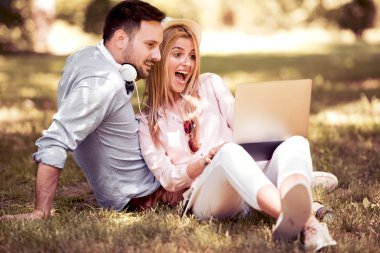 Birlikte parkta oturan ve dizüstü bilgisayar kullanarak genç Çift