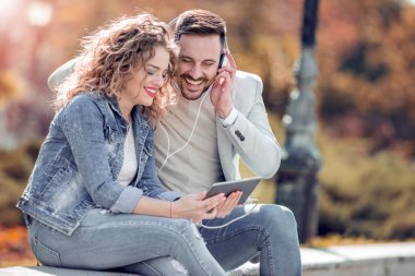 Açık havada eğleniyor ve gülümseyerek, tablet üzerinde seyir mutlu genç Çift.