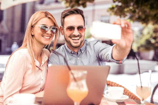 Man and woman sitting in street cafe and making selfie