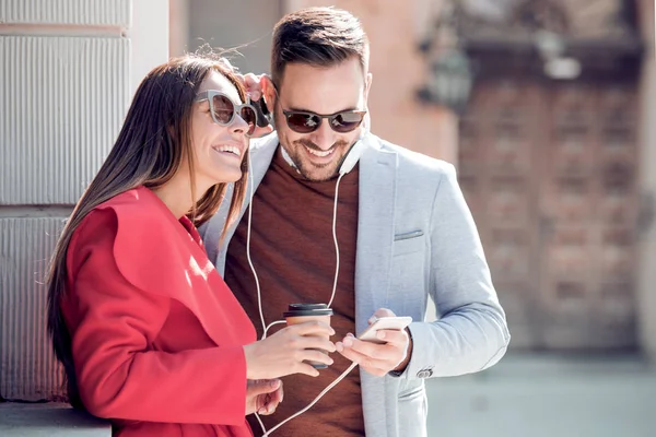 Happy couple with headphones sharing music from smartphone on street