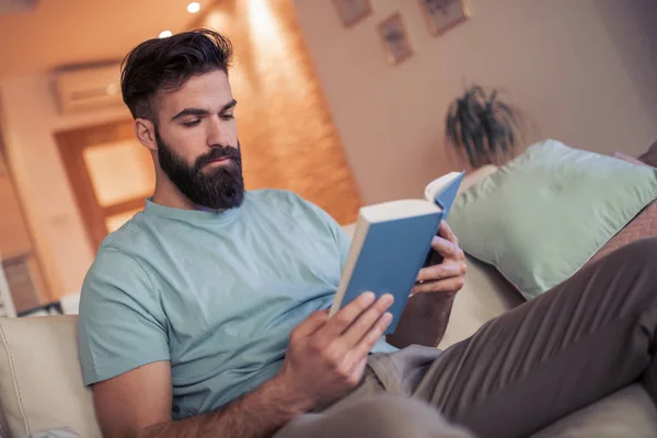 Joven Sentado Sofá Leyendo Libro Casa — Foto de Stock