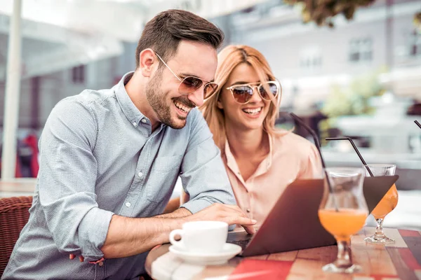 Man and woman sitting in street cafe and browsing laptop