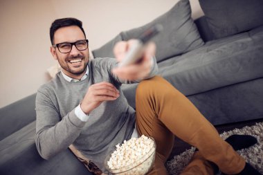 Genç adam evde kanepe üzerinde patlamış mısır ile TV izleme